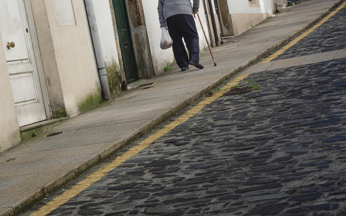 Escena cortada de un señor con bastón y una bolsa en la mano subiendo una cuesta en San Pedro.