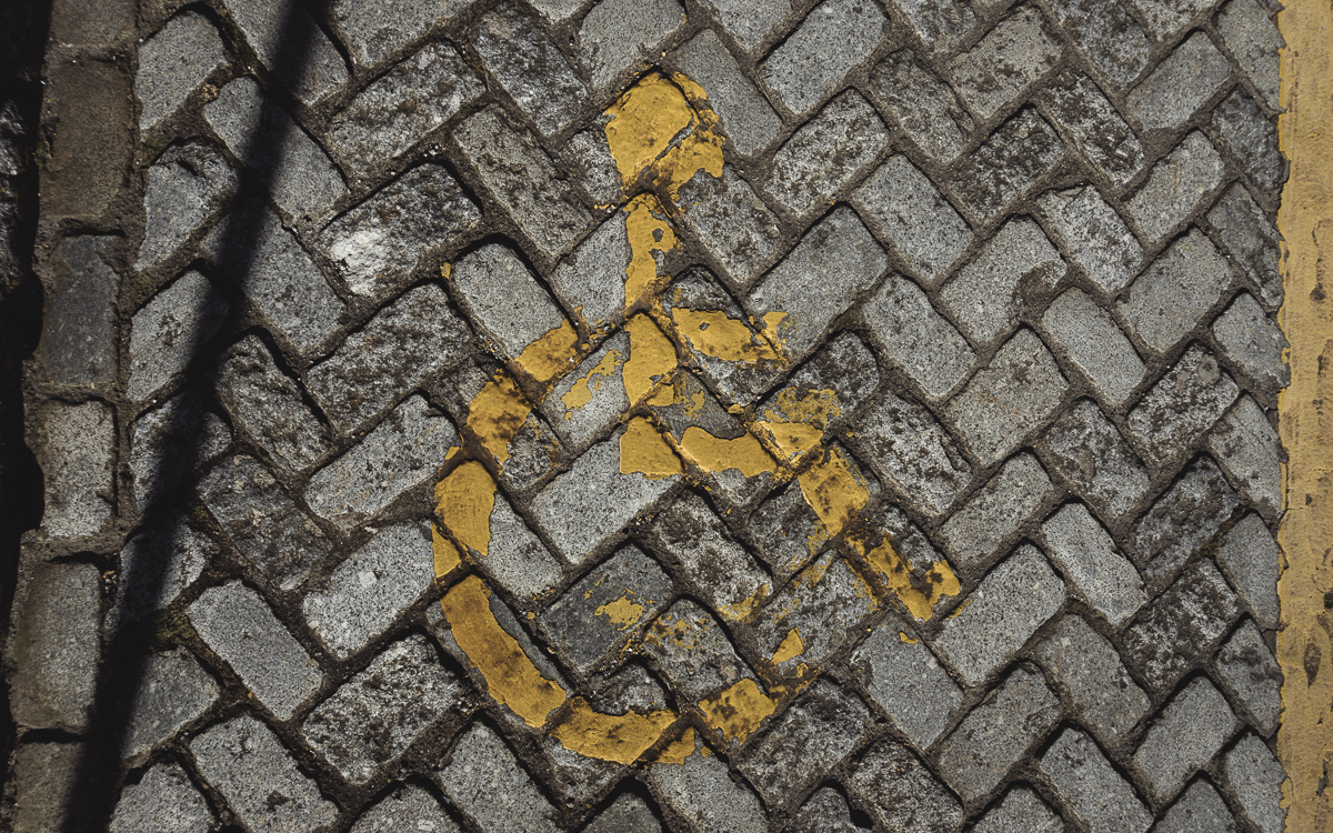 Suelo adoquinado con señal de "reservado para personas con movilidad reducida" muy deteriorada.