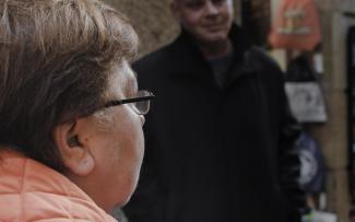 Primer plano del perfil de una mujer conversando con un hombre cuya silueta aparecere desenfocada.