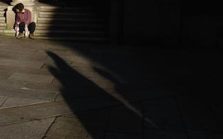 Composición artística de mujer sentada en escaleras de piedra iluminada y rodeada de sombra.
