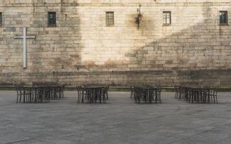 Mesas de hostelería vacías y cruz católica de fondo en la Plaza de Quintana dos Mortos.