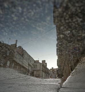 Imagen artística del reflejo en un charco, de una calle transitada del casco antiguo de Santiago.