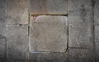 Pavimento lítico con huecos y desniveles en el que se observa incrustado un pequeño papel doblado.