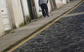 Escena cortada de un señor con bastón y una bolsa en la mano subiendo una cuesta en San Pedro.