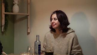 Plano medio de mujer sentada en una mesa de un restaurante sonriendo maliciosamente.